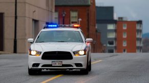 A white municipal Dodge Charger police car flashes its lights before participating in a high-speed chase.