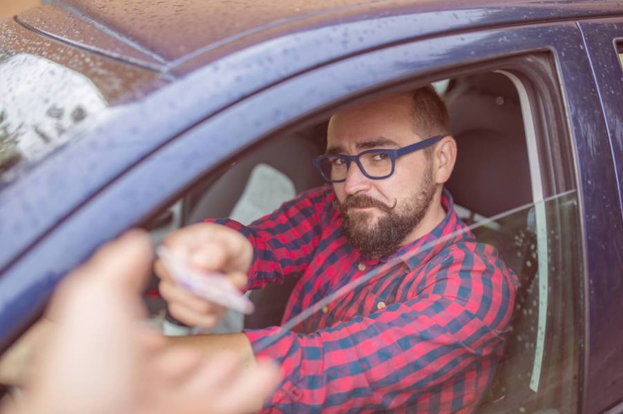 A driver hands over their driver's license to a police officer after rolling the car window down halfway.