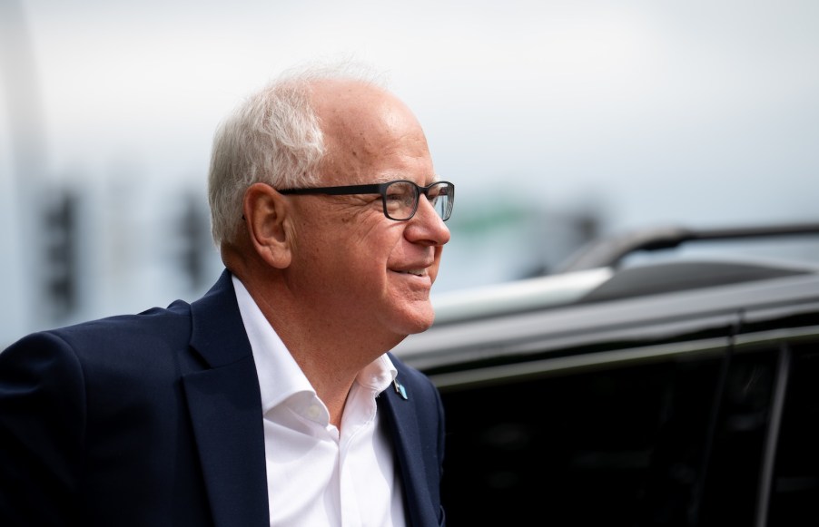 Governor Tim Walz stands in front of a black SUV.