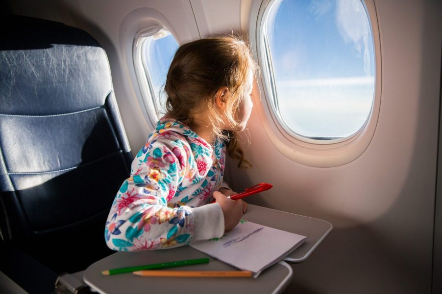 Kid looking out the window of an airplane while drawing a picture.