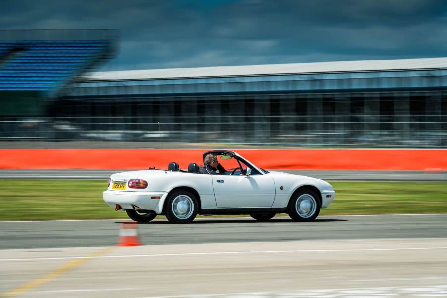 An NA Mazda MX-5 Miata drives around a track like the Nürburgring or Silverstone.