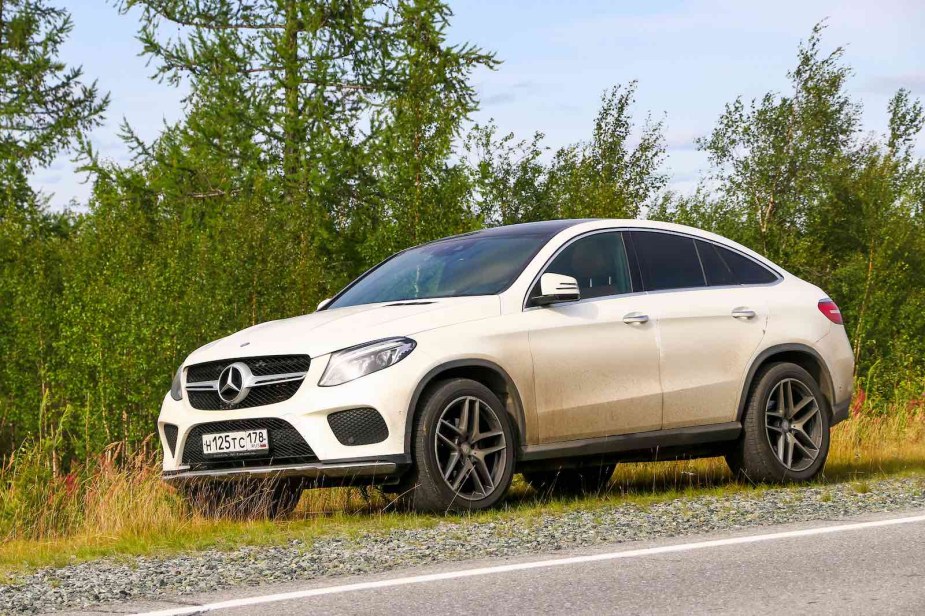 White Mercedes coupe SUV parked by the roadside, trees visible in the background.