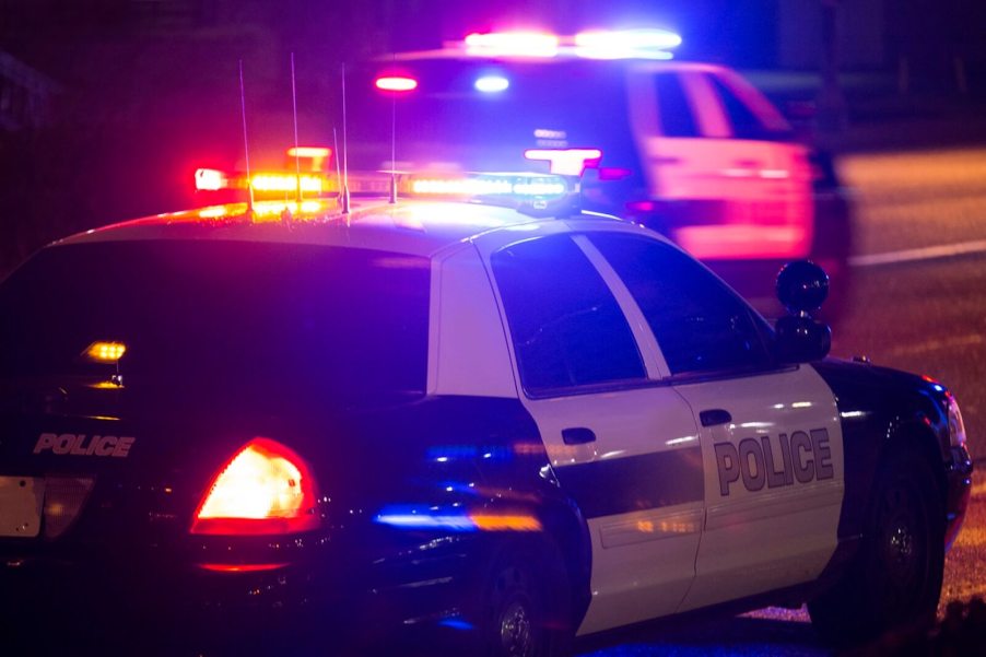 Police officers driving a Ford Crown Victoria prepare to deploy spike strips to stop a chase.