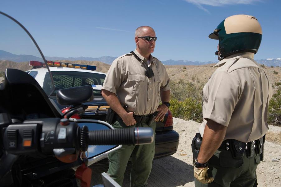 Two police officers stand by the road side and talk.