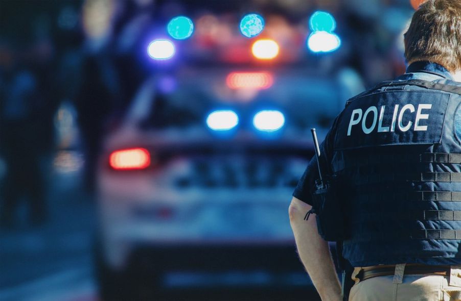 A police officer stands at an emergency scene listening to a police scanner and his radio.