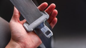 A driver's hand holding a seatbelt buckle in a state where they must be buckled up.