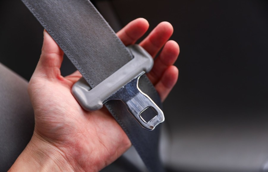 A driver's hand holding a seatbelt buckle in a state where they must be buckled up.