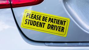 Bright yellow bumper sticker for a student driver, on the back of a silver hatchback.