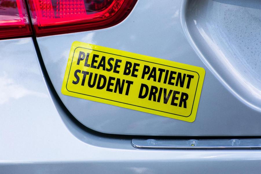 Bright yellow bumper sticker for a student driver, on the back of a silver hatchback.