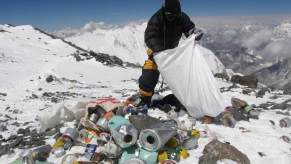 Sherpa loads trash in a plastic bag on Everest, the Himalaya visible in the background.