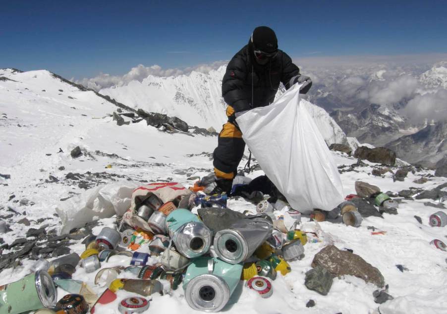 Sherpa loads trash in a plastic bag on Everest, the Himalaya visible in the background.