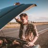 Man looks under the hood of his pickup truck parked by the highway.