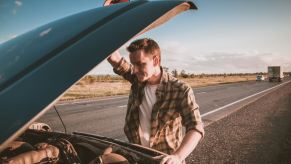 Man looks under the hood of his pickup truck parked by the highway.