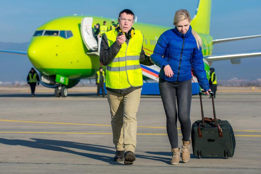 Airport manager leading a detained woman away from an airplane.