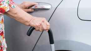 An elderly person's hand on a car door handle and cane in the other