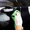 Car detailer hand wearing white latex glove wiping black car exterior door with a green microfiber cloth in close view