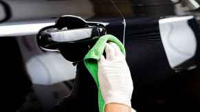 Car detailer hand wearing white latex glove wiping black car exterior door with a green microfiber cloth in close view