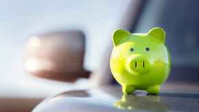 A green piggy bank sitting on a car hood in close view depiction of a car loan