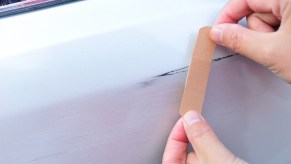 A scratch on a car in close view with hands placing a band-aid over it you might consider avoiding a car insurance claim for small damage