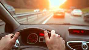 Driving on a highway from driver perspective hands on steering wheel at sunset