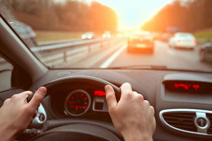 Driving on a highway from driver perspective hands on steering wheel at sunset