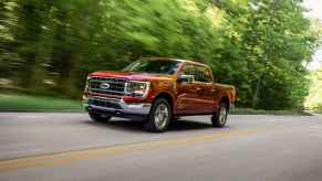 A red Ford F-150 pickup truck driving in left angle view on a two-lane road with blurred trees behind