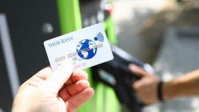 White credit card held in front of a green gas pump.