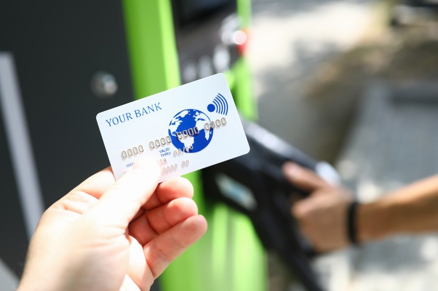 White credit card held in front of a green gas pump.