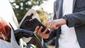 Man holding iPhone close to a charging EV five states allow using your Apple Wallet to store driver's license in 2024