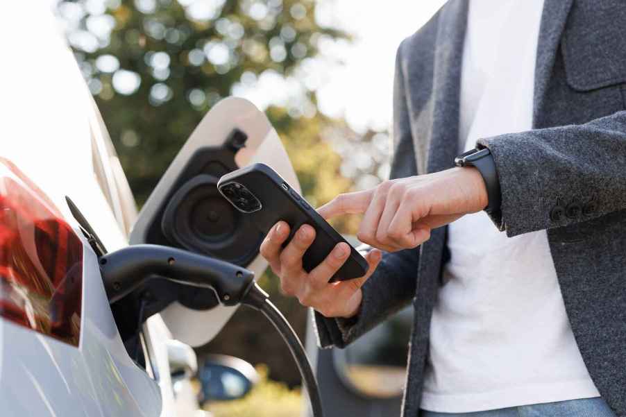 Man holding iPhone close to a charging EV five states allow using your Apple Wallet to store driver's license in 2024