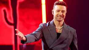 Justin Timberlake on stage wearing grey suit jacket right arm outstretched