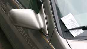 A parking ticket on a silver car's windshield tucked under the right wiper blade in close view