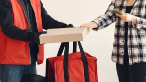 Pizza delivery driver hands pizza box to woman holding cash people are shown from neck to knees