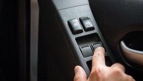 A handle pressing a button on a car's power window switch with "auto" feature in close view