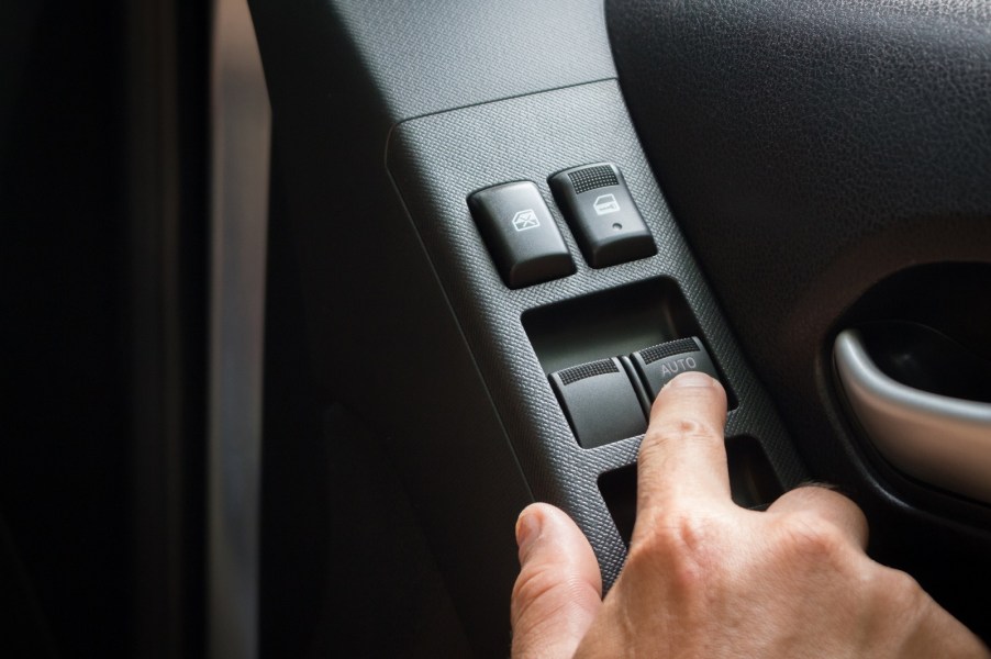 A handle pressing a button on a car's power window switch with "auto" feature in close view