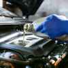 Automotive tech at Quick Lube facility wearing blue gloves fills car with oil in very close view