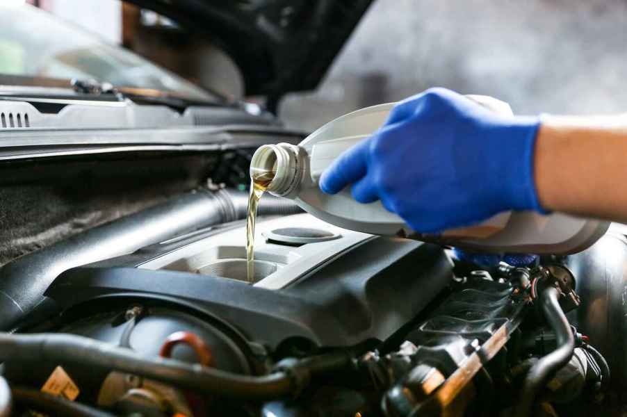 Automotive tech at Quick Lube facility wearing blue gloves fills car with oil in very close view