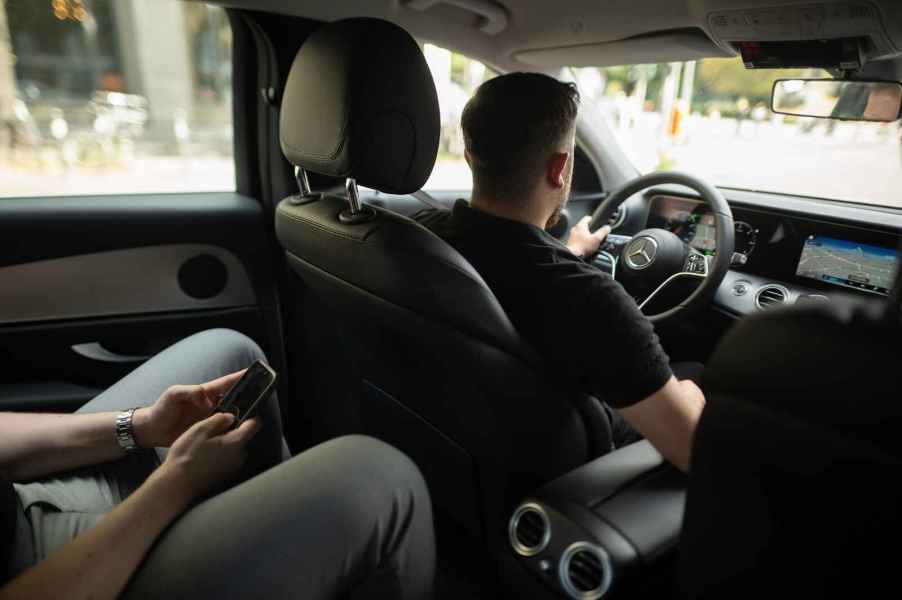 An Uber driver and left rear passenger holding a cell phone inside a Mercedes vehicle from right rear passenger view