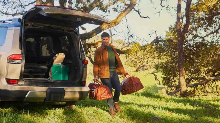 2024 Lexus GX driver carries his luggage through a grassy field, his SUV visible in the background.