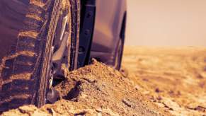 The tires of a silver vehicle buried in the sand, and trapped in the desert.