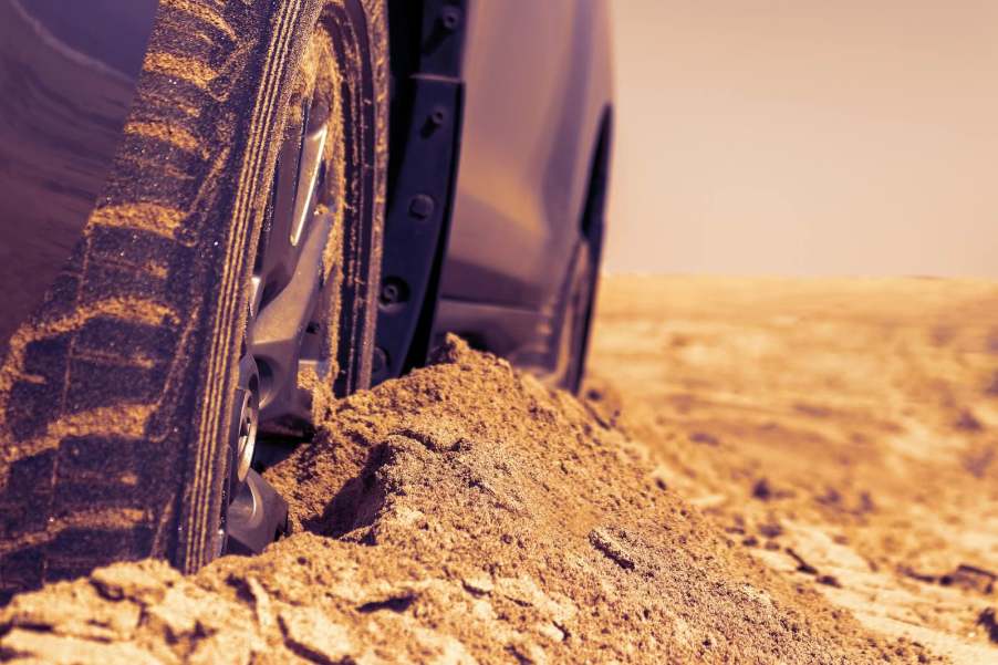 The tires of a silver vehicle buried in the sand, and trapped in the desert.