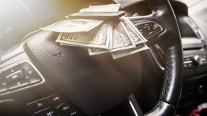 Stack of $100 bills set on the steering wheel of a car.