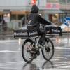 Bicycle deliver rider with a dominos back in a parka in a rainy city