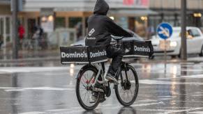 Bicycle deliver rider with a dominos back in a parka in a rainy city