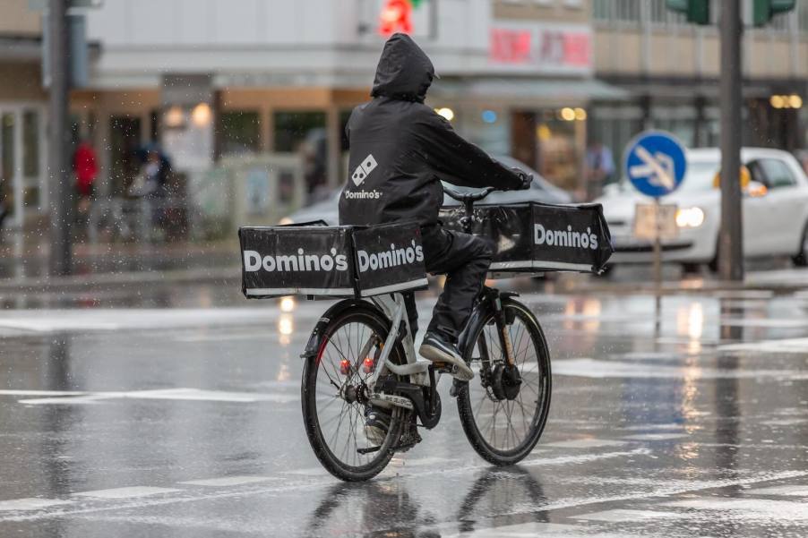 Bicycle deliver rider with a dominos back in a parka in a rainy city