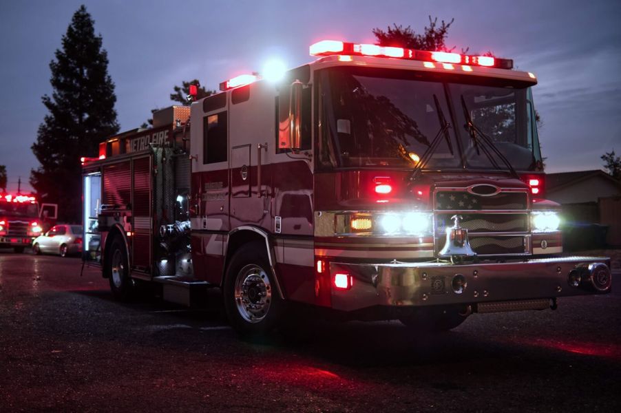 This fire truck sits at a scene with its lights on and gear intact.