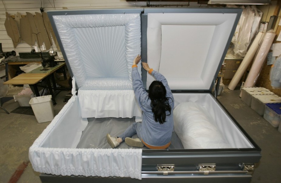 Goliath Caskets employee shapes the interior of a 48-inch extra-large steel casket in a workshop.