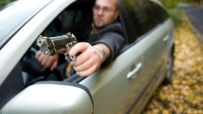 Angry driver holds a gun out the window of his car.