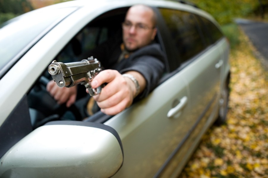 Angry driver holds a gun out the window of his car.