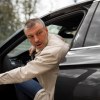 Man in a white shirt leans out the door of a formal car.